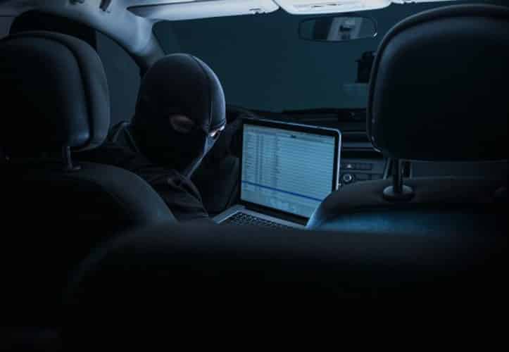 Scary man in a mask using his laptop to hack a business in a car